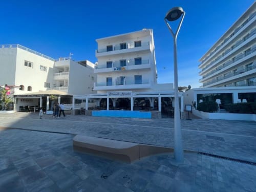 Plaza frente al mar Apartamentos Playa Sol en Es Canar con edificio residencial blanco y restaurante con vistas al Mediterráneo