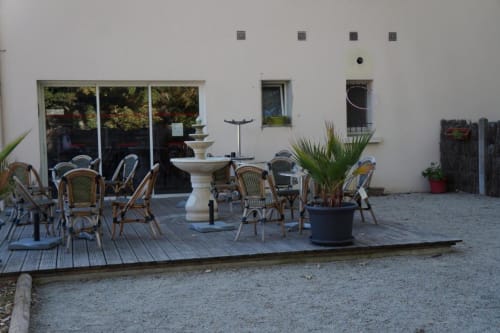 Terrasse extérieure de l'Hôtel Bar La Pinède avec fauteuils en rotin, fontaine et façade blanche à Saint-Jean-de-Monts