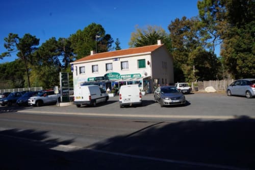 Hôtel Bar La Pinède à Saint-Jean-de-Monts : bâtiment blanc, toit en terre cuite, voitures garées et arbres environnants