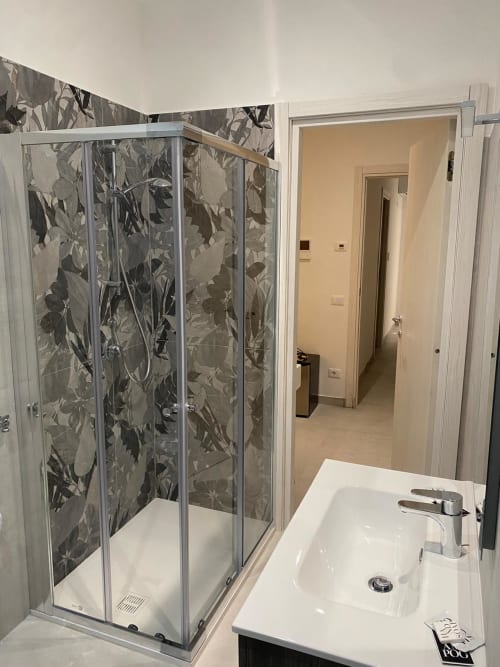 Modern bathroom with glass shower enclosure featuring floral pattern, white sink, and chrome faucet at Rose room in
