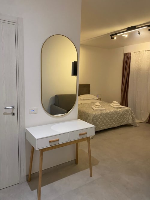 Modern bedroom at RL GROUP hotel with oval mirror, vanity desk, and bed with white linens in Civitanova del Sannio