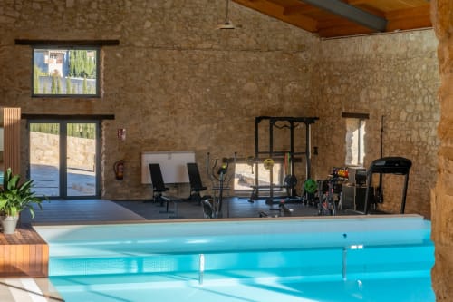 Indoor swimming pool at El Batán Hotel Spa in Castillo de Locubín with gym equipment and stone walls