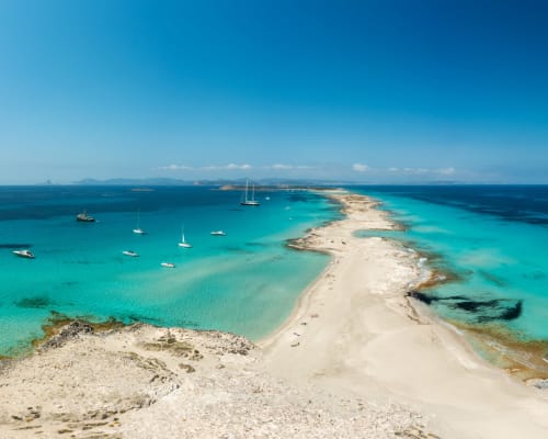 Aguas turquesas y playa de arena en Es Canar con veleros fondeados cerca de Apartamentos Playa Sol