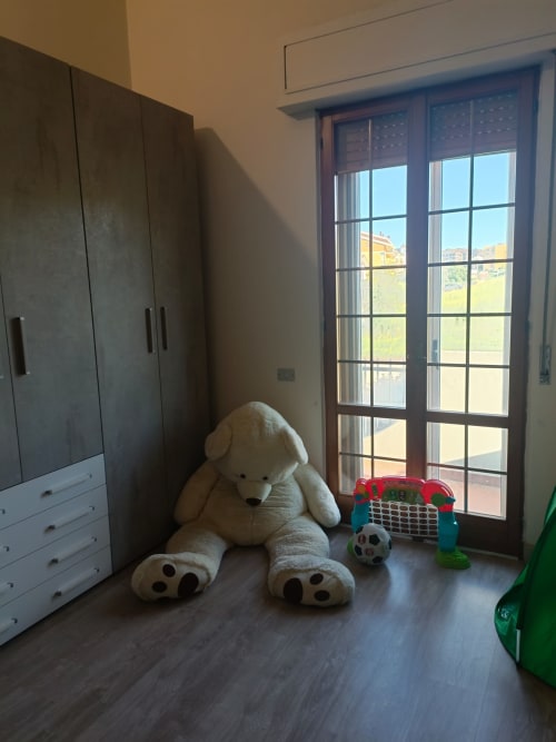 Child's bedroom in Atessa apartment with large stuffed bear, toys, wooden flooring, wardrobe, and glass doors overlooking