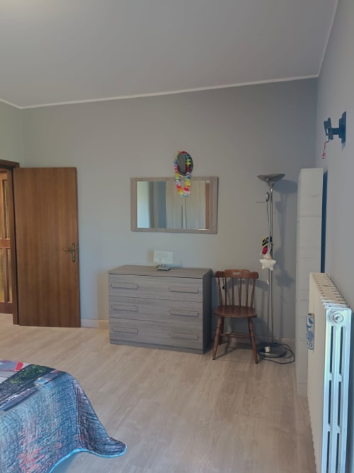 Bright bedroom in Atessa apartment with dresser, wooden chair, mirror, radiator, and bed
