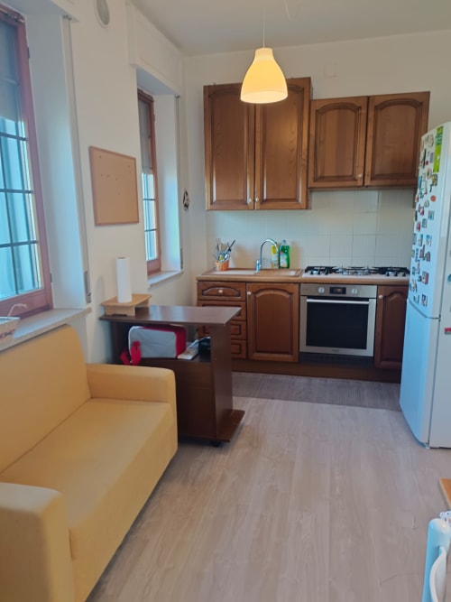 Modern kitchen-living area in Atessa apartment with wooden cabinets, stainless steel appliances, yellow sofa, and pendant