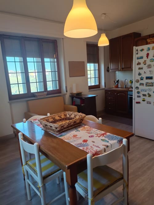Bright dining area in Atessa apartment with wooden table, white chairs, pendant lights, and city view windows