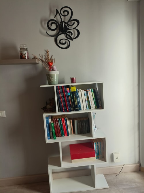 Modern white bookshelf with organized books, decorative plants, and spiral wall clock in Atessa apartment