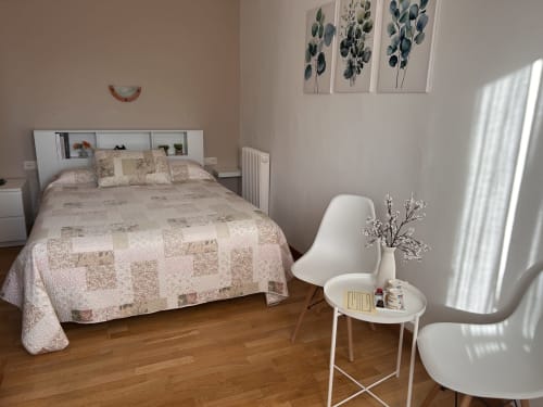 Bright double bedroom at Hostal Estació in Puigcerdà with patchwork bedding, white modern chair, wooden floors, and botanical