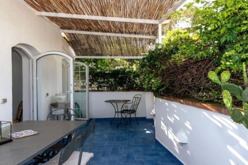 Terrazza coperta di La Conciergerie Capri con pavimento in majolica blu, posti a sedere all'aperto e vista sul lussureggiante giardino
