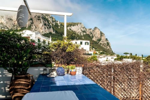 Terrazza sul tetto di La Conciergerie Capri con piastrelle blu, piante in vaso e vista spettacolare delle scogliere calcaree