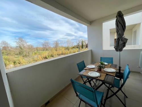 Zona pranzo su balcone della Résidence Marina di Bravone con tavolo in terrazza, sedie turchesi e vista sul paesaggio costiero