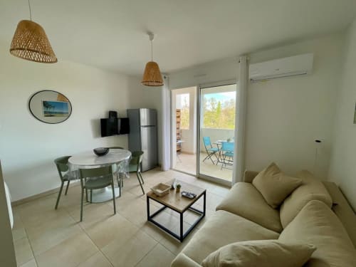 Accogliente appartamento T2 a Résidence Marina di Bravone con divano beige, tavolo da pranzo e balcone vista mare