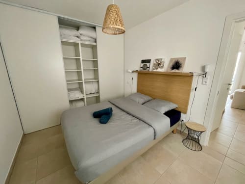 Camera moderna e accogliente a Résidence Marina di Bravone con letto in legno, pareti bianche, lampada a sospensione in vimini e scaffali