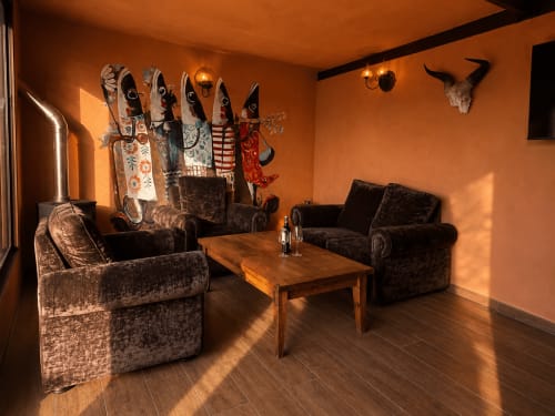 Aconchegante salão em tons quentes com assentos em veludo escuro, mesa de madeira, máscaras decorativas e vista para as montanhas no hotel Jardines de Ifonche