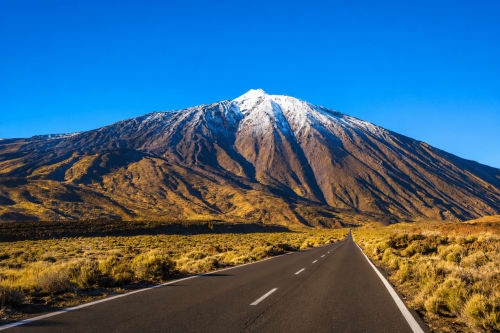 Straight road leading to snow-capped volcano in arid landscape near Tenerife