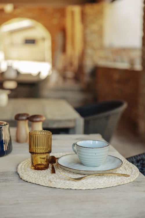 Elegant place setting at Mas Tihou with light blue ceramic cup, white plate, and amber glass on woven placemat
