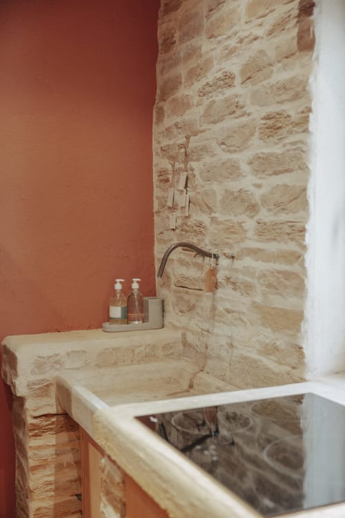Rustic stone sink in Mas Tihou room with terracotta wall and brass faucet in Le Beausset