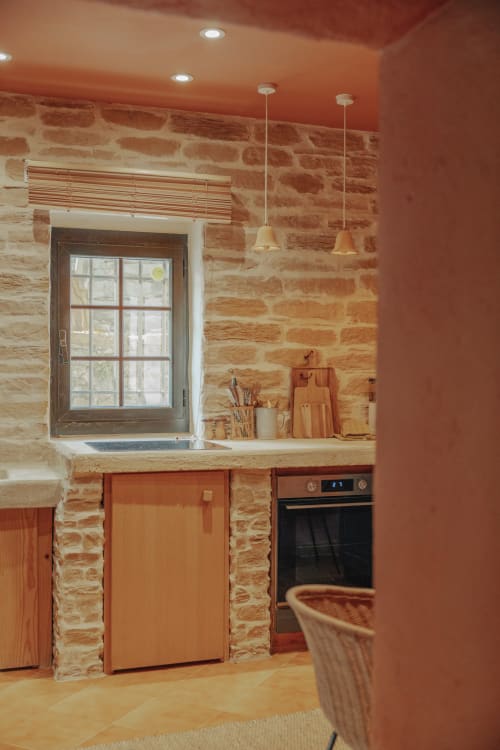 Modern kitchen with terracotta brick walls, pendant lights, and window at Mas Tihou B&B in Le Beausset, France