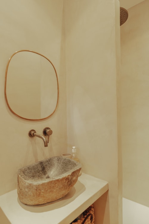 Rustic stone sink with copper faucet and round mirror in Mas Tihou B&B bathroom, Le Beausset