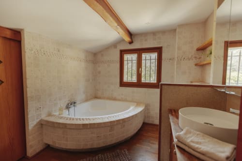 Spacieuse salle de bain du gîte Mas Tihou avec baignoire d'angle jacuzzi, lavabo indépendant, poutres en bois et vue sur jardin