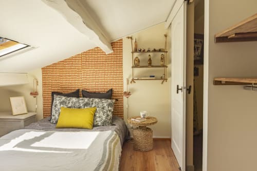 Chambre cosy à Mas Tihou avec coussin jaune, papier peint géométrique orange, étagères en bois et vue sur le jardin