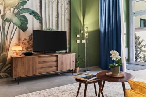 Salotto moderno Nestco Milano con mobili in legno, TV, pareti verdi, tende blu e vista giardino