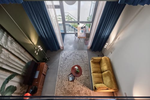 Moderno loft a Milano con divano giallo, tavolino rosso e vista sul giardino attraverso ampie finestre a tutta altezza con blu