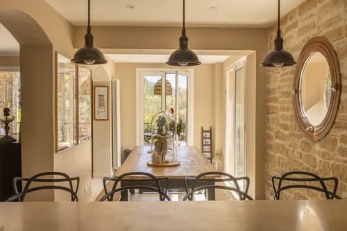Salle à manger moderne du gîte Mas Tihou au Beausset avec luminaires suspendus, mur en pierre et portes donnant sur le jardin