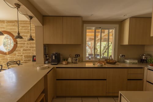 Cuisine moderne avec meubles en bois, mur en pierre et vue sur le jardin du gîte Mas Tihou au Beausset