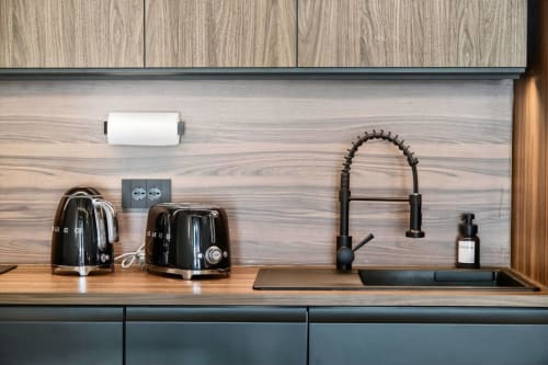Bancone cucina moderno presso Nestco Milano con elettrodomestici neri, macchina espresso e elegante schienale in legno in The Loft Jenner