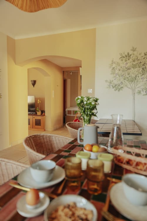 Salle à manger du gîte Mas Tihou au Beausset avec table dressée, chaises en osier et cuisine jaune visible