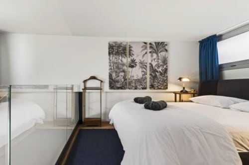 Camera da letto Loft Jenner a Milano con biancheria bianca, arte botanica alle pareti, tende blu e comfort moderni