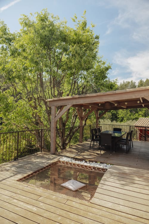 Terrasse en bois du gîte Mas Tihou avec pergola, coin repas, foyer encastré et vue sur jardin luxuriant au Beausset