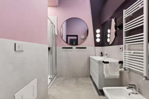 Bagno moderno in The Loft Jenner, Milano. Pareti rosa e scure, specchi rotondi, lavabo bianco, doccia, portasciugamani e riscaldato