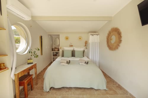 Chambre lumineuse et moderne du gîte Mas Tihou au Beausset avec lit queen, salle de bain attenante, miroir rond et vue sur le jardin.