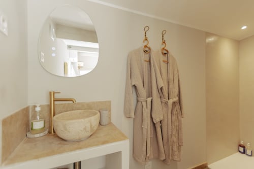 Salle de bain élégante du gîte Mas Tihou au Beausset avec miroir rond, lavabo en pierre et deux peignoirs beige aux crochets