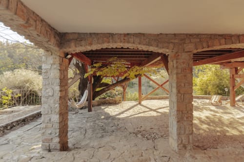Pergola rustique en pierre avec poutres en bois au gîte Mas Tihou au Beausset, vue sur jardin avec hamac et transats
