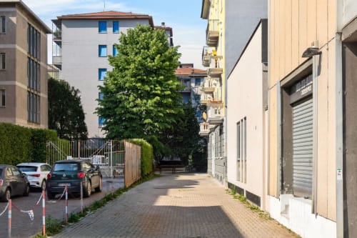 Cortile Nestco Milano con auto parcheggiate, albero rigoglioso e moderni edifici residenziali con finestre blu