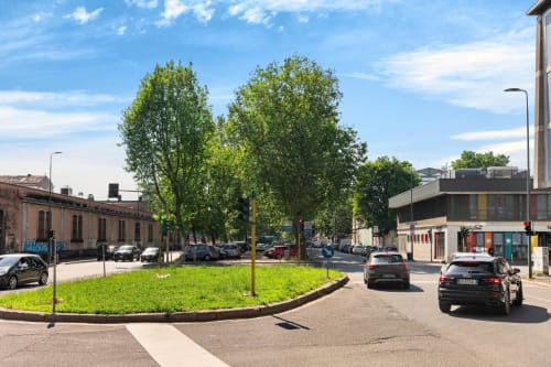 Cortile urbano a Milano con prato verde, alberi e auto parcheggiate vicino al complesso residenziale Nestco
