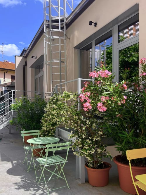 Il giardino di The Loft Jenner a Milano con fiori rosa, arredi bistrot verdi e moderna facciata dell'edificio