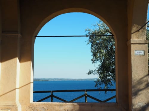 Finestra in pietra ad arco con vista sul Lago di Garda, edera e acque blu dall'hotel Prince Garda, Salò