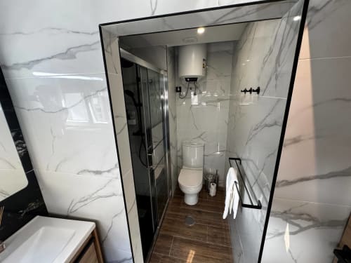 Banheiro moderno na villa Antas Family Retreat com paredes em mármore, box de vidro, sanitário e piso em madeira escura