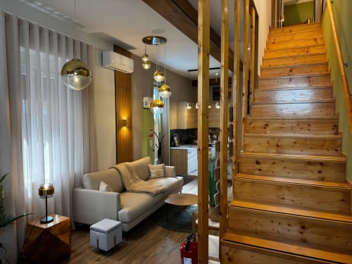 Área de estar moderna com sofá cinzento, iluminação pendente, escadas de madeira e vistas da cidade na vila Amber Star Rent em Vila Nova de