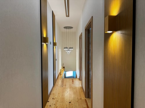 Corredor moderno na villa Antas Family Retreat com piso em madeira, iluminação pendente e detalhes em tons âmbar na Amber
