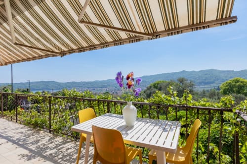 Sonnige Terrasse der Casa Zolia Mendia mit gelben Stühlen, gestreifter Markise und Blick auf die Berge des Gardasees, Salò