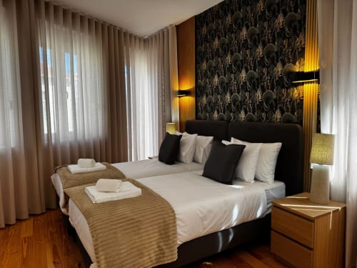 Suíte luxuosa na villa Antas Family Retreat com cama estofada em preto, roupas de cama creme, parede com padrão decorativo e iluminação âmbar sofisticada