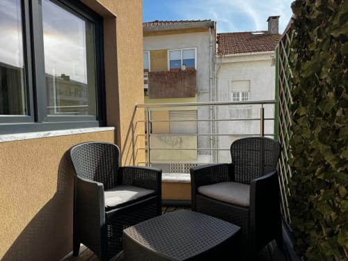 Cadeiras de vime preto na varanda ensolarada da villa Antas Family Retreat em Vila Nova de Gaia com vista para a cidade e hera
