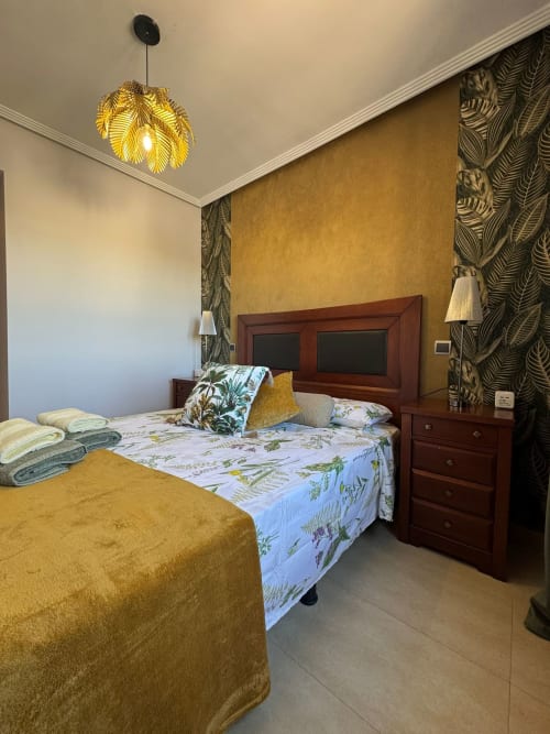 Dormitorio en apartamento Haus Holiday Homes, San Pedro del Pinatar, con lámpara colgante dorada y papel pintado estampado tropical
