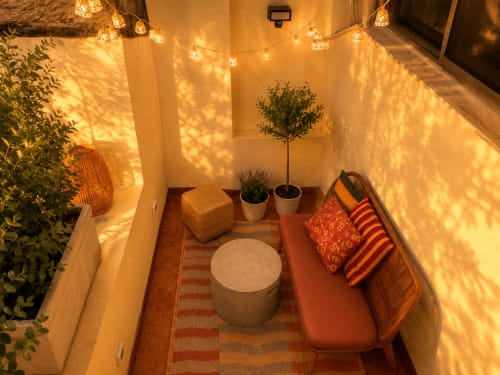 Terrazza accogliente dell'appartamento Domus Beato Angelico a Roma con luci soffuse, piante in vaso, divano rosso e sedute intrecciate